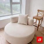 Bright modern room interior showcasing a luxury round accent chair upholstered in soft off white bouclé fabric featuring cylindrical armrests and a matching throw pillow by Bahoo Furniture UAE