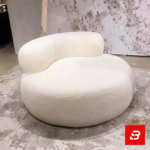 Bright modern room interior showcasing a luxury round accent chair upholstered in soft off white bouclé fabric featuring cylindrical armrests and a matching throw pillow by Bahoo Furniture UAE