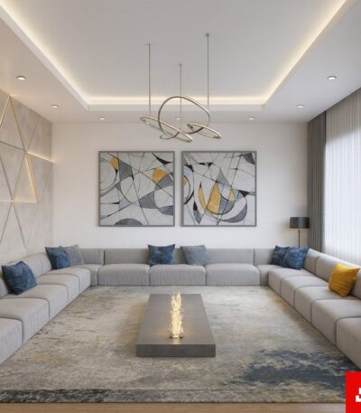 Front interior view of a luxury upholstered modern majlis sectional sofa in warm gray velvet fabric featuring blue and yellow accent pillows and a central fire feature table by Bahoo Furniture UAE