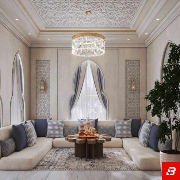 Front interior view of a luxury upholstered modern majlis sectional sofa in beige velvet fabric featuring blue accent cushions and an ornate wooden coffee table by Bahoo Furniture UAE