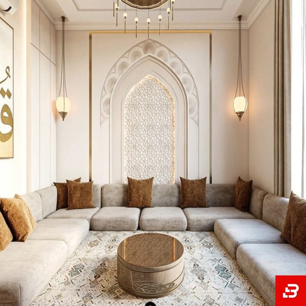 Eye-level interior view of a luxury upholstered arabic majlis sectional sofa in warm gray velvet fabric featuring brown accent pillows and an ornate arched wall feature by Bahoo Furniture UAE