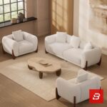 Stylized living room interior view of a luxury upholstered contemporary sofa set featuring a 3-seater sofa and two matching armchairs in off white bouclé fabric with dark wooden base accents by Bahoo Furniture UAE