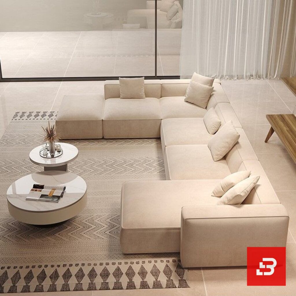High-angle interior view of a luxury upholstered grand modular sectional sofa in beige velvet fabric featuring dual chaise extensions and accent pillows by Bahoo Furniture UAE