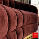Sophisticated modern living room interior showcasing a luxury channel-tufted sofa upholstered in soft beige velvet fabric featuring a rounded curved back and a gold metallic base plinth by Bahoo Furniture UAE