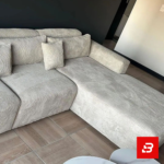 Contemporary modern living room interior showcasing a plush l-shape sectional sofa upholstered in ribbed warm gray textured corduroy paired with nested marble coffee tables against a dark accent wall by Bahoo Furniture UAE