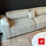 Contemporary modern living room interior showcasing a plush l-shape sectional sofa upholstered in ribbed warm gray textured corduroy paired with nested marble coffee tables against a dark accent wall by Bahoo Furniture UAE