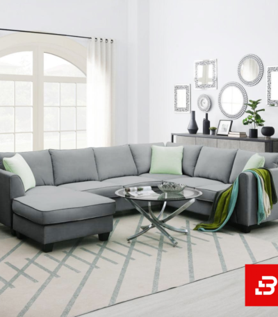 Bright and airy modern living room interior showcasing a large l-shape sectional sofa upholstered in soft warm gray fabric with pastel green throw pillows and a glass coffee table by Bahoo Furniture UAE
