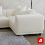 Luminous classic living room interior showcasing an off white bouclé l-shape sectional sofa with a matching ottoman, vintage chandelier, and marble accent wall by Bahoo Furniture UAE