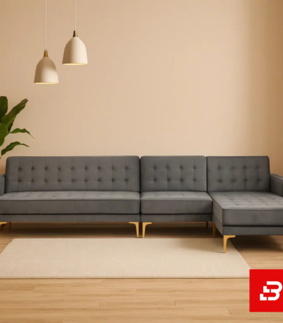 Warmly lit modern living room interior showcasing a warm gray fabric tufted l-shape sectional sofa with deep button tufting, gleaming gold metal legs, pendant lights, and indoor plant by Bahoo Furniture UAE
