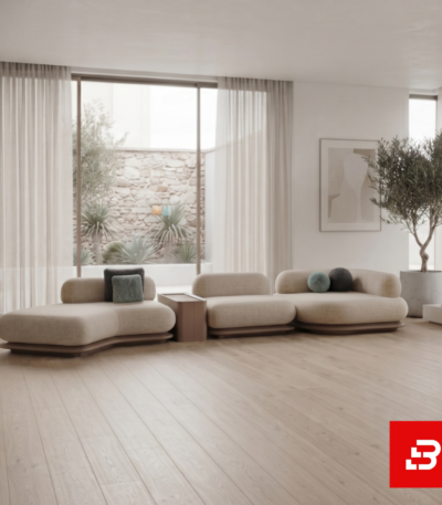 Sunlit minimal living room interior showcasing a sweeping curved modular sectional sofa upholstered in soft beige bouclé fabric with a wooden console table and sheer curtains by Bahoo Furniture UAE