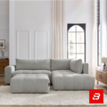 Bright modern living room interior featuring a warm gray fabric tufted l-shape sectional sofa with vertical channel tufting, matching footrest ottoman, and arched window by Bahoo Furniture UAE
