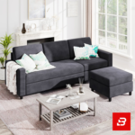 Bright modern living room interior showcasing a warm gray fabric l-shape sectional sofa with matching footrest ottoman, patterned botanical scatter pillows, a wooden coffee table, and a fireplace mantel by Bahoo Furniture UAE
