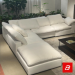 Serene modern luxury living room interior showcasing a plush l-shape sectional sofa upholstered in soft off white fabric paired with a matching chaise lounge and indoor botanical plants by Bahoo Furniture UAE