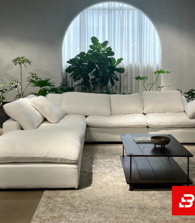 Serene modern luxury living room interior showcasing a plush l-shape sectional sofa upholstered in soft off white fabric paired with a matching chaise lounge and indoor botanical plants by Bahoo Furniture UAE
