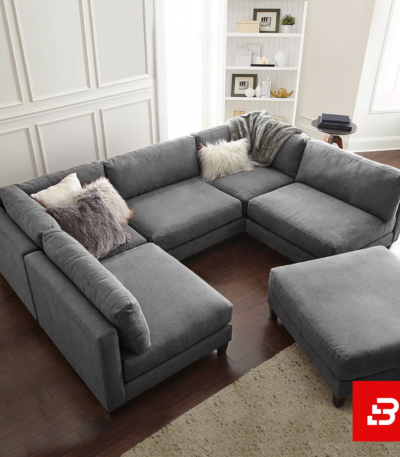 Overhead view of a modern luxury living room interior showcasing a grand u-shape sectional sofa upholstered in soft warm gray textured fabric with plush faux-fur accent pillows and matching ottoman by Bahoo Furniture UAE