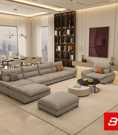 Elegant modern luxury living room interior showcasing a spacious contemporary sectional sofa with an attached chaise lounge upholstered in soft warm gray fabric with matching orange accent cushions by Bahoo Furniture UAE